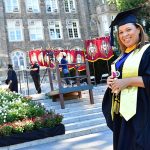 A woman graduate poses in front of the steps of Keating Terrace