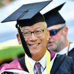 A male graduate with classes smiling