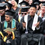 Graduates with aqua and white stoles chatting in audience